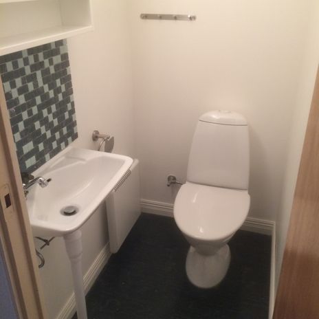 Toalettrum med vit wc-stol. vitt handfat, grön mosaik ovanför handfatet, vita väggar