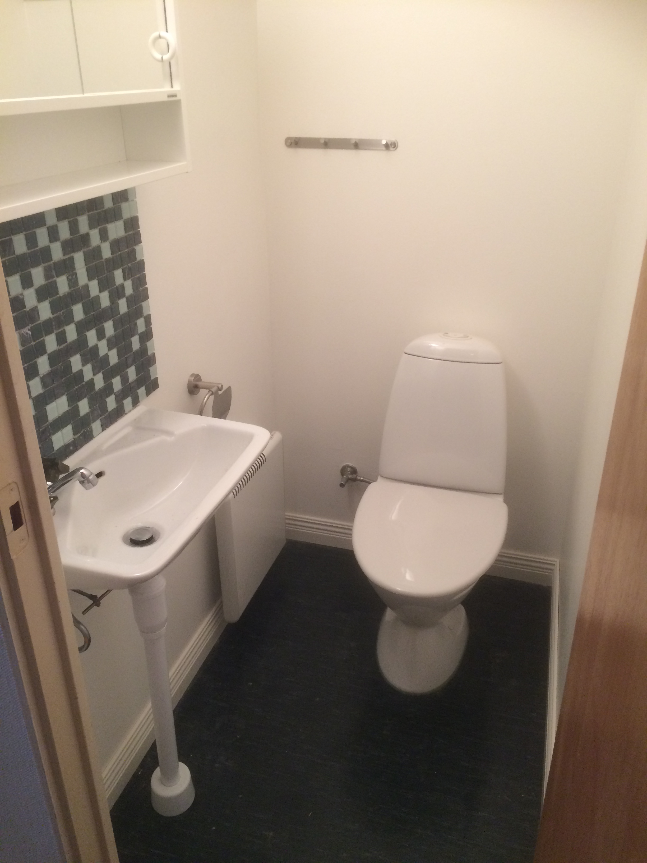 Toalettrum med vit wc-stol. vitt handfat, grön mosaik ovanför handfatet, vita väggar