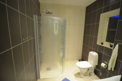 Duschrum med vit kaklad vägg, två gråkaklade väggar, duschdörr i frostat glas.
