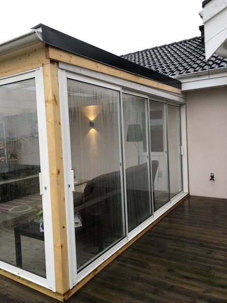 Uterum i glas på en trädäckad altan, svart utemöbler.