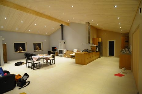 Stort allrum med högt i tak, trätak med spotlights, kakelugn, matgrupp - bord med duk på samt svarta stolar