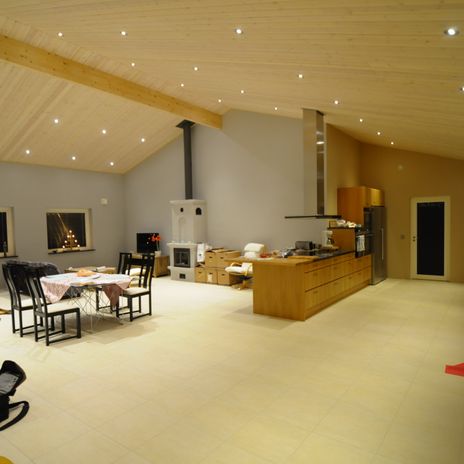 Stort allrum med högt i tak, trätak med spotlights, kakelugn, matgrupp - bord med duk på samt svarta stolar