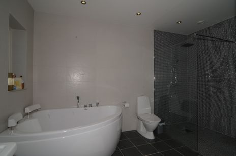 Vitt badrum med vitt hörnbadkar, vit wc-stol, glasduschvägg